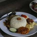 a white plate topped with rice and meat