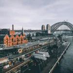 aerial photography of concrete buildings and bridge beside ocean under cloudy sky